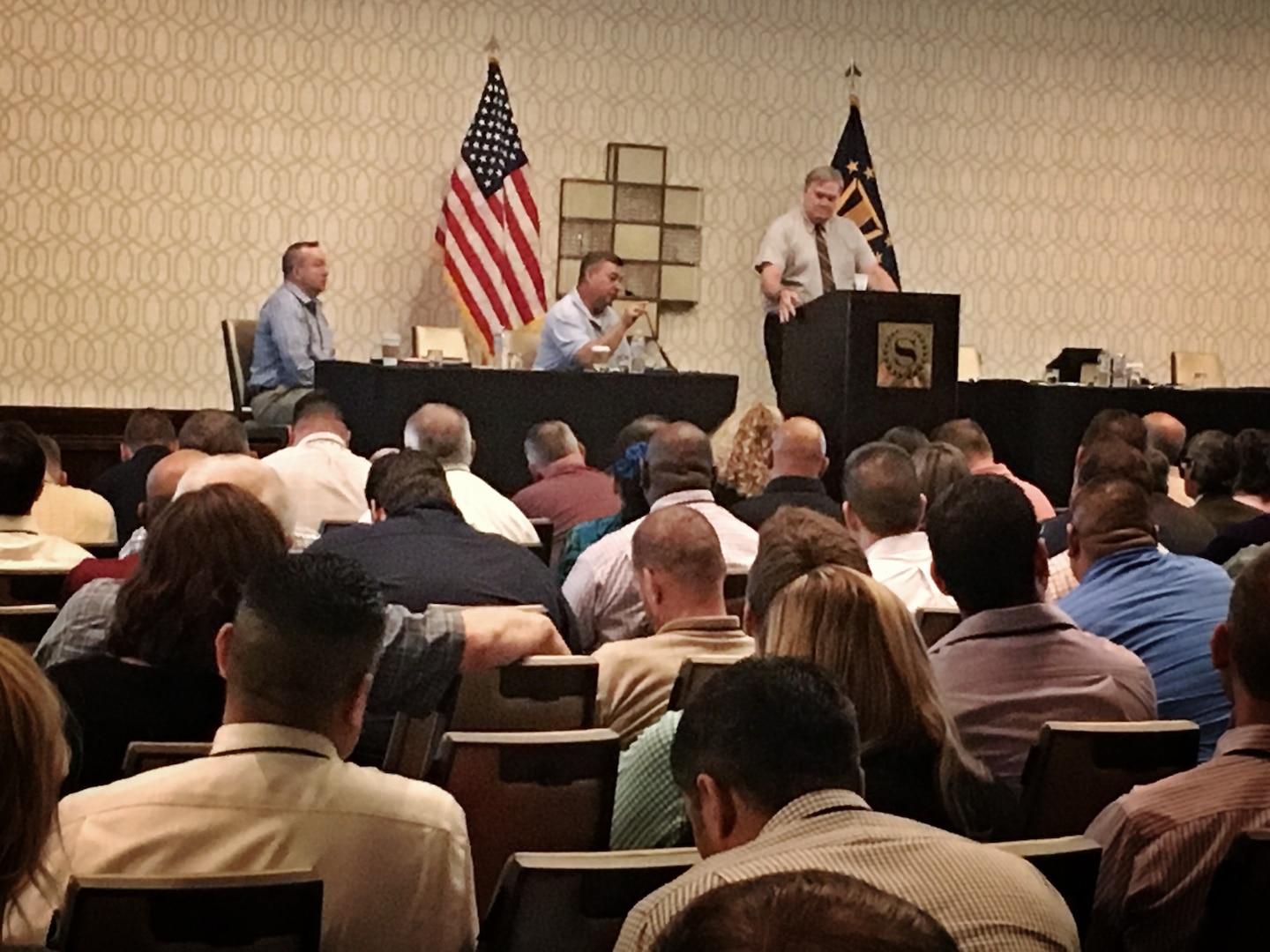 Group of people listen to a man speaking at a podium