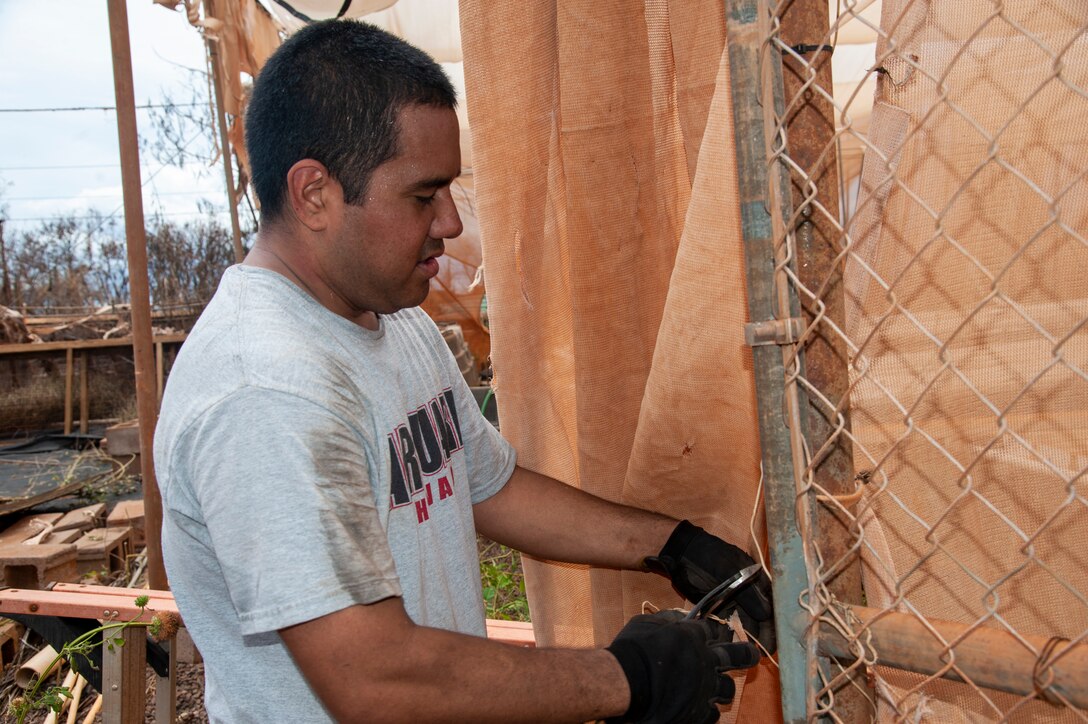 Master Sgt. Jeremy Akima, 292nd Combat Communications Squadron cyber surety craftsman, cuts canvas from a damaged aquapponics structure at Lahainaluna High School