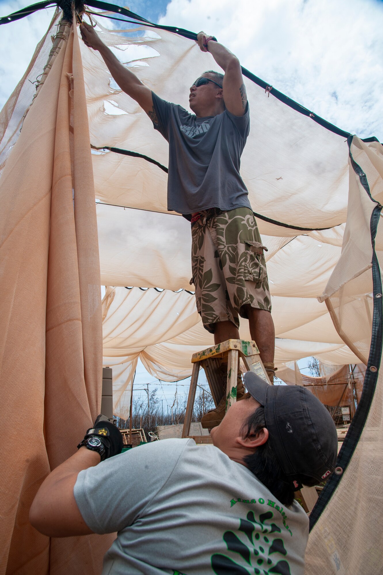1st Sgt. Marlon Domingo (top) with the 230th Engineering Battalion secures canvas on a damaged aquapponics structure while wife, Master Sgt. Shannon Domingo with the 292nd Combat Communications Squadron secures the ladder at Lahainaluna High School
