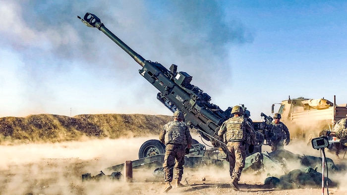 Soldiers approach a Howitzer after it is fired in the desert.