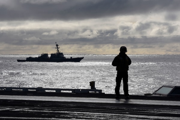 A sailor stands on the flight deck of the aircraft carrier USS Harry S. Truman during flight operations in the North Atlantic as the guided missile cruiser USS Normandy sails alongside.