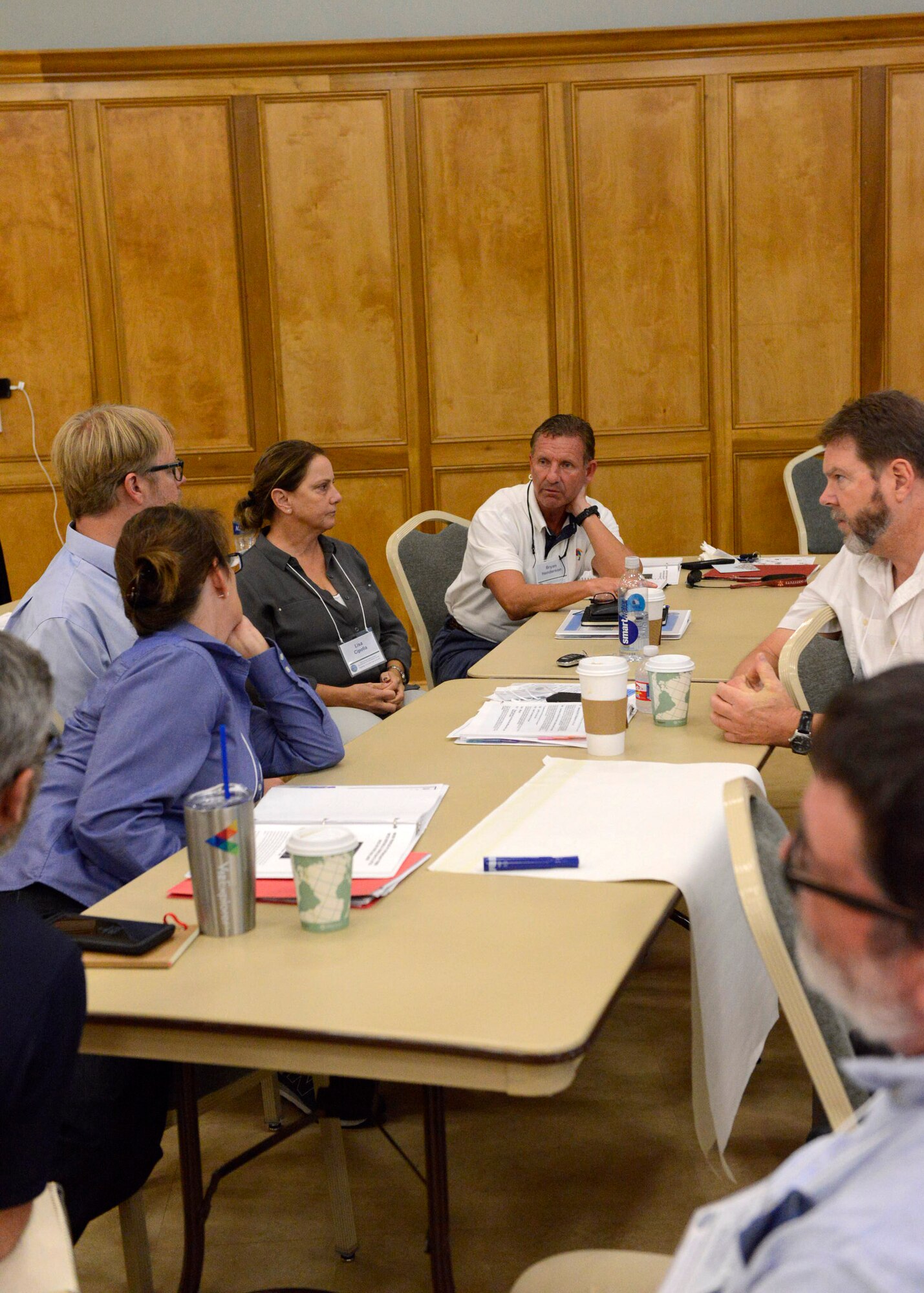 A group of white males and females sit around a long table and discuss a scenario and how to deal with it.