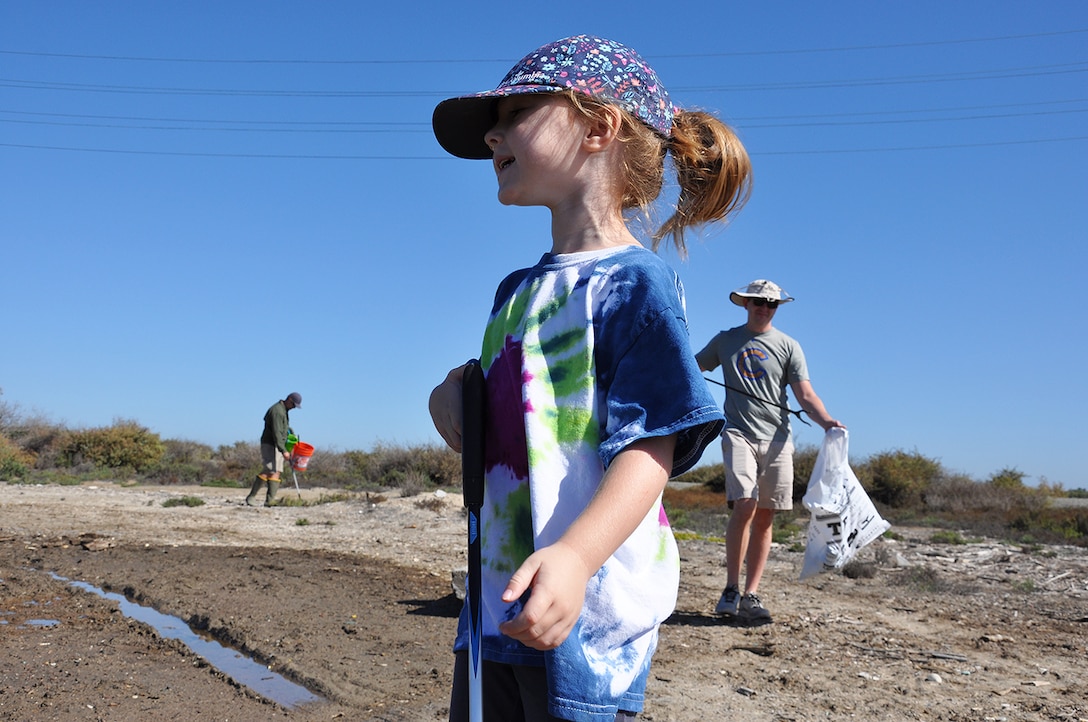 Amelia Jones, 4, foreground, looks off into the distance, as her father, Chris, background left, and her uncle, Andrew Hardison, background right, pick up trash during the Santa Ana River Marsh Cleanup Day Sept. 15 in Newport Beach, California. The event was part of California Coastal Cleanup Day.