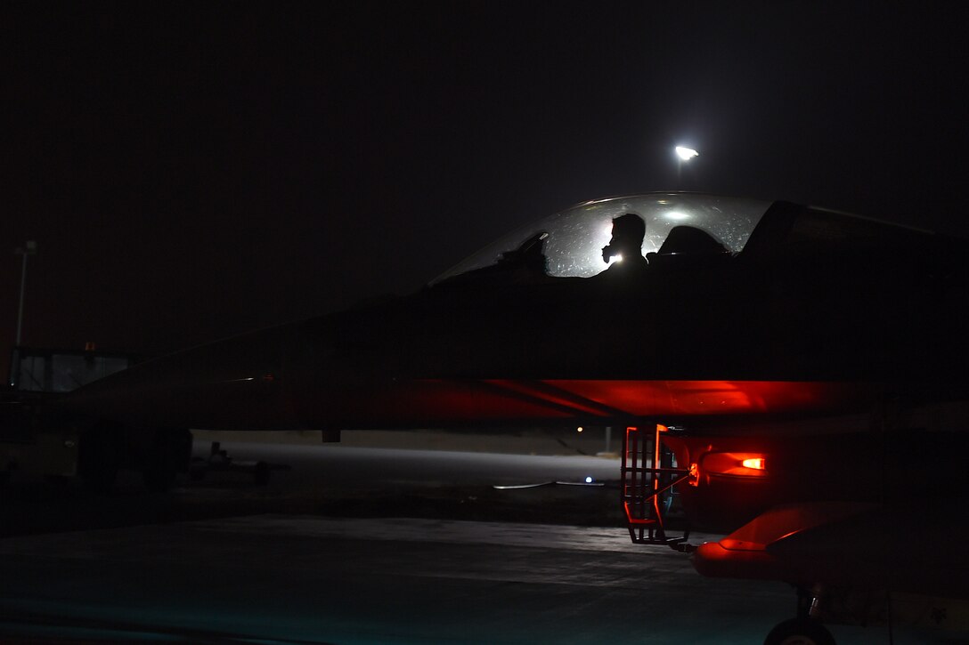 An Airmen sits in the cockpit if and F-16 Fighting Falcon on the flightline at night