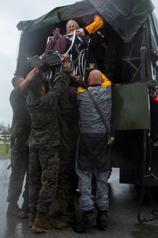 Marines help an elderly woman in a wheelchair out of a vehicle assisting first emergency responders.