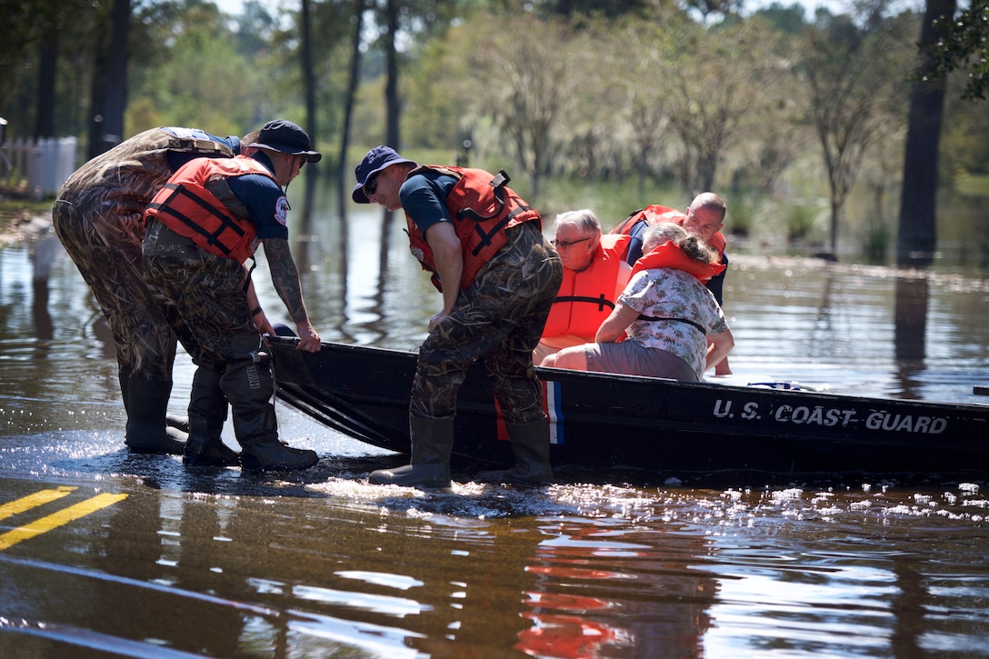 Members of the Coast Guard’rescue an elderly couple from floodwaters in a boat.