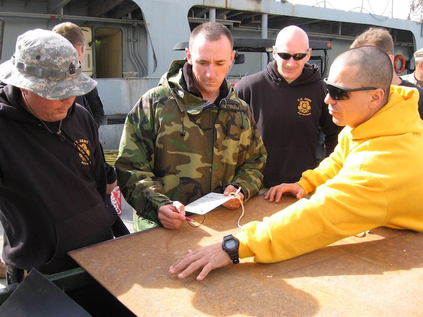 Foster with CPT Dan Curtin and 1SG Rodney Heikkinen discussing how best to build and apply a patch to a US Coast Guard cutter along the Persian Gulf, again with 7th Engineer Dive Detachment [Heavy Salvage]. The vessel collided with a submerged metal buoy, and suffered