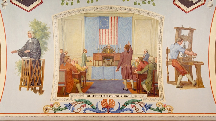 A painting shows a man in colonial garb standing and gesticulating in a room with seated men and an early U.S. flag adorning a wall.