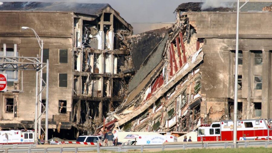 A destroyed section of a Pentagon facade is sandwiched by intact sections, with fire vehicles parked in front.