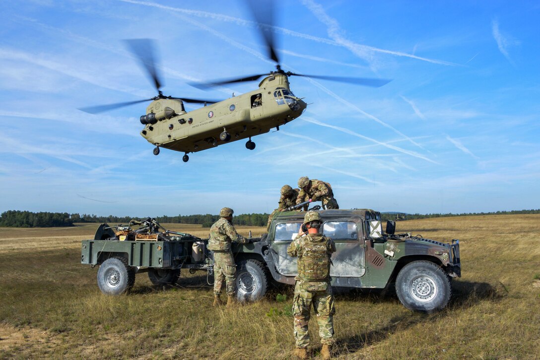 A soldier documents unit members sling-load a Humvee and trailer to a CH-47 Chinook helicopter.