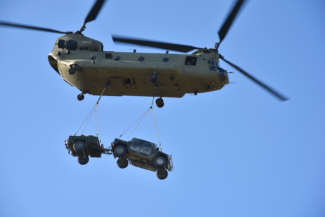 A CH-47 Chinook helicopter lifts off sling-loading a Humvee and trailer.