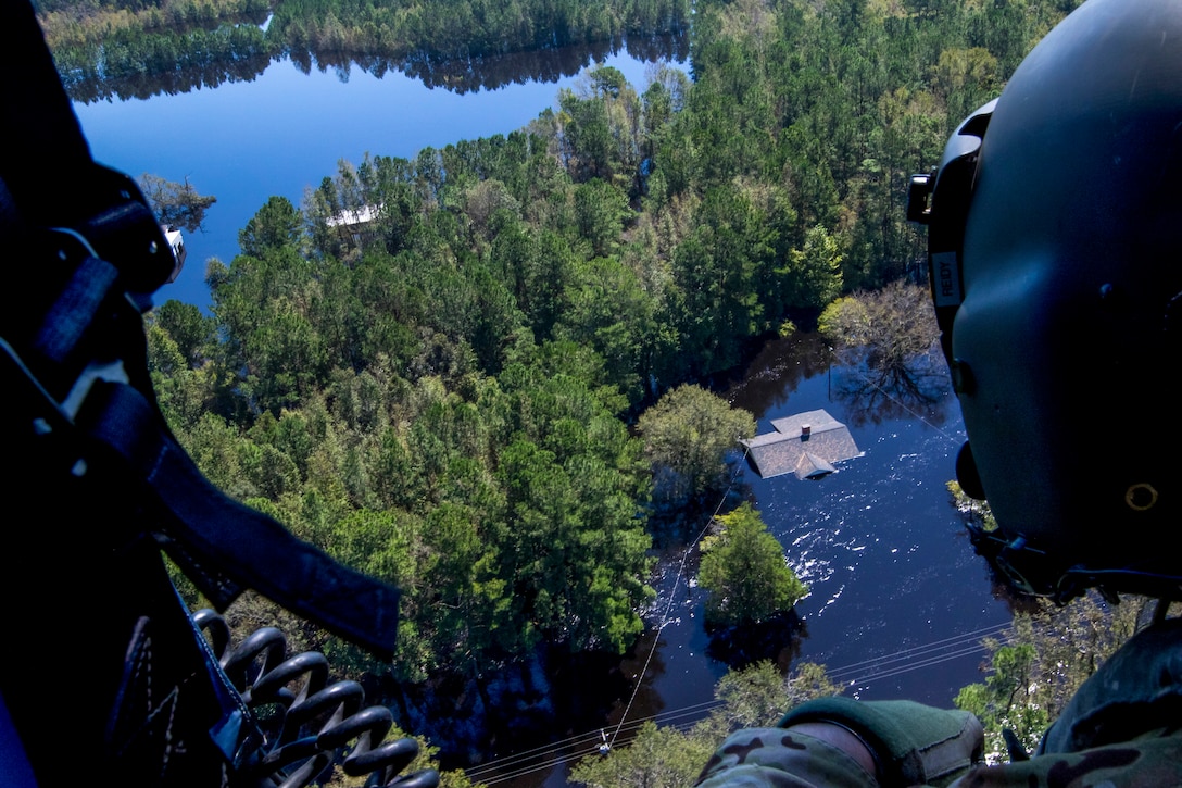 A soldier looks out over a flooded area from a helicopter.