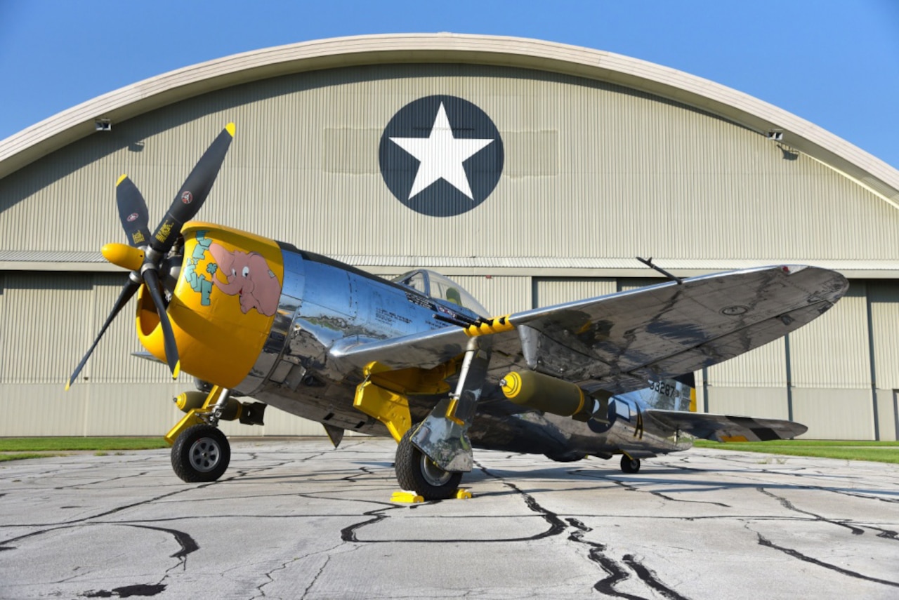 A vintage plane sits next to a hangar.