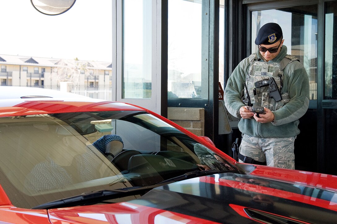 An airman checks an ID at a military base gate.
