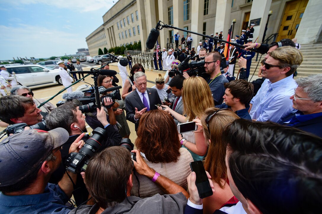 Defense Secretary James N. Mattis talks outside the Pentagon while surrounded by reporters with cameras and microphones.