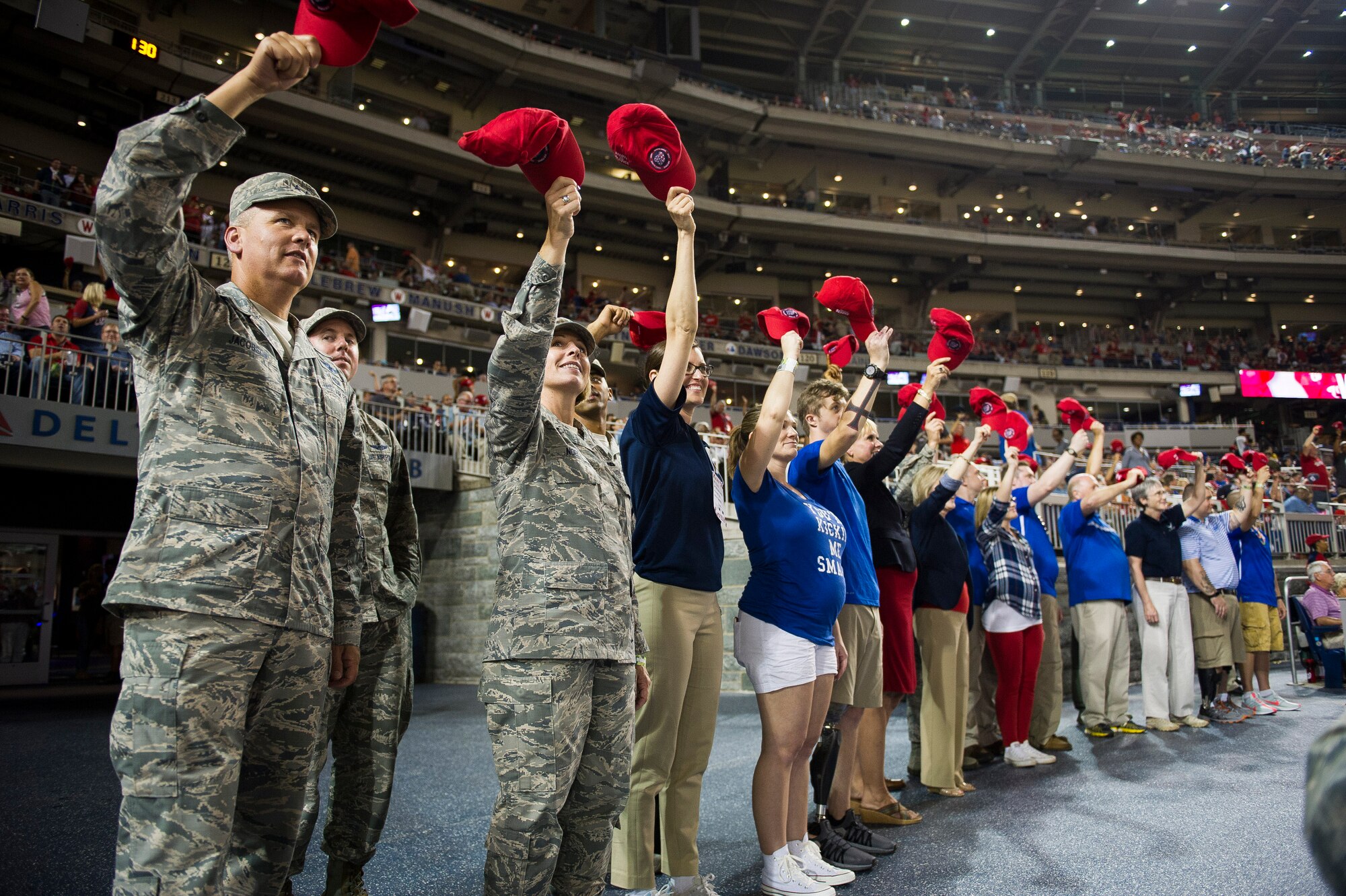 A group of Airmen and their families wave red hats to a crowd at the baseball game.
