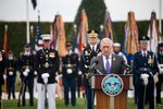 Defense Secretary James N. Mattis speaks at a lectern on a parade field, as troops stand behind him.