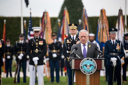 Defense Secretary James N. Mattis speaks at a lectern in front of troops on a parade field.
