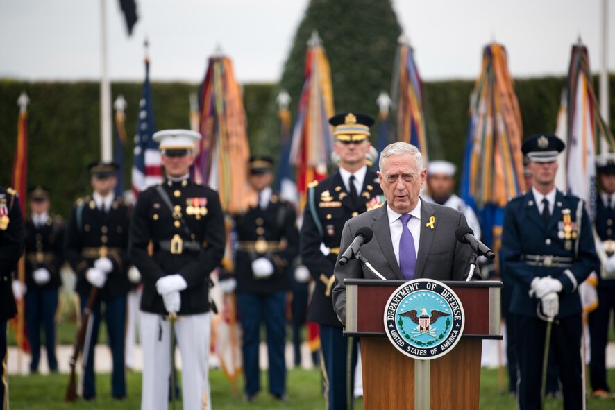 Defense Secretary James N. Mattis speaks at a lectern in front of troops on a parade field.
