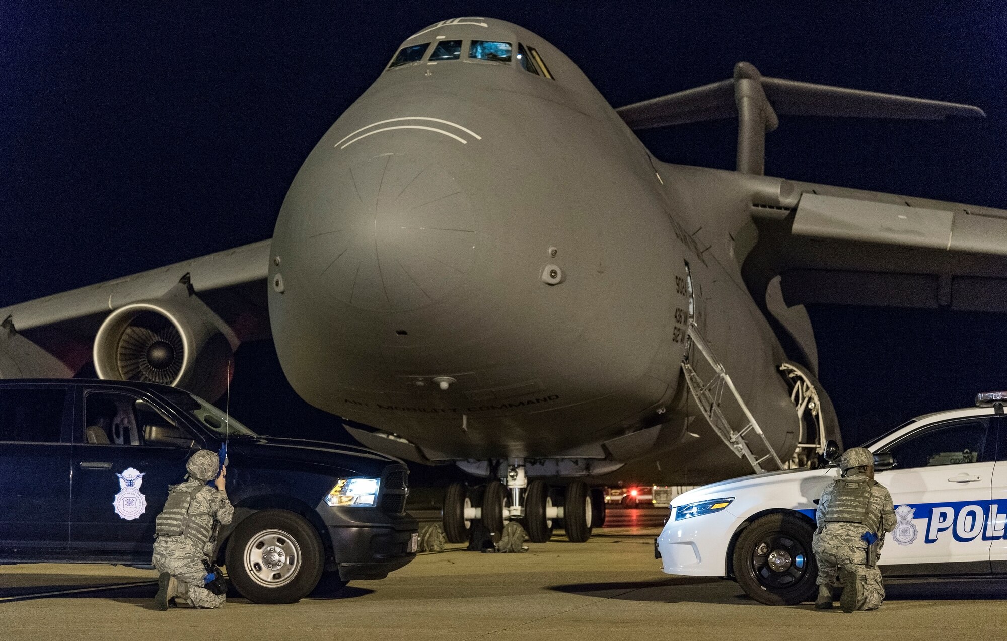 Two 436th Security Forces Squadron response force members take cover behind their vehicles positioned in front of a C-5M Super Galaxy as part of anti-hijacking measures Sept. 17, 2018, on Dover Air Force Base, Del. More than 20 response force members and other first responders positioned themselves and vehicles around the C-5M in response to a simulated attempted hijacking and hostage scenario. (U.S. Air Force photo by Roland Balik)