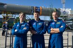 A U.S., Russian and Canadian astronaut pose in front of a Soyuz rocket.