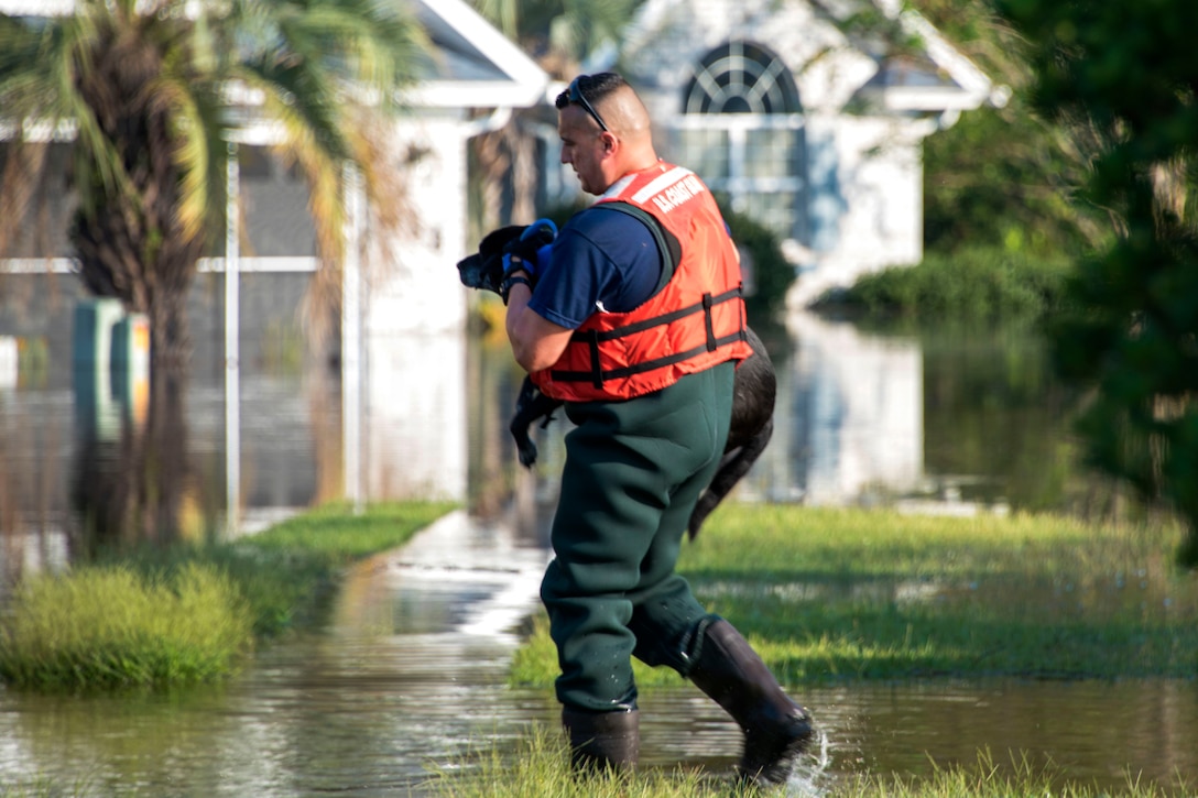 A U.S. Coast Guard member carries a dog after being rescuing through a flooded neighborhood.