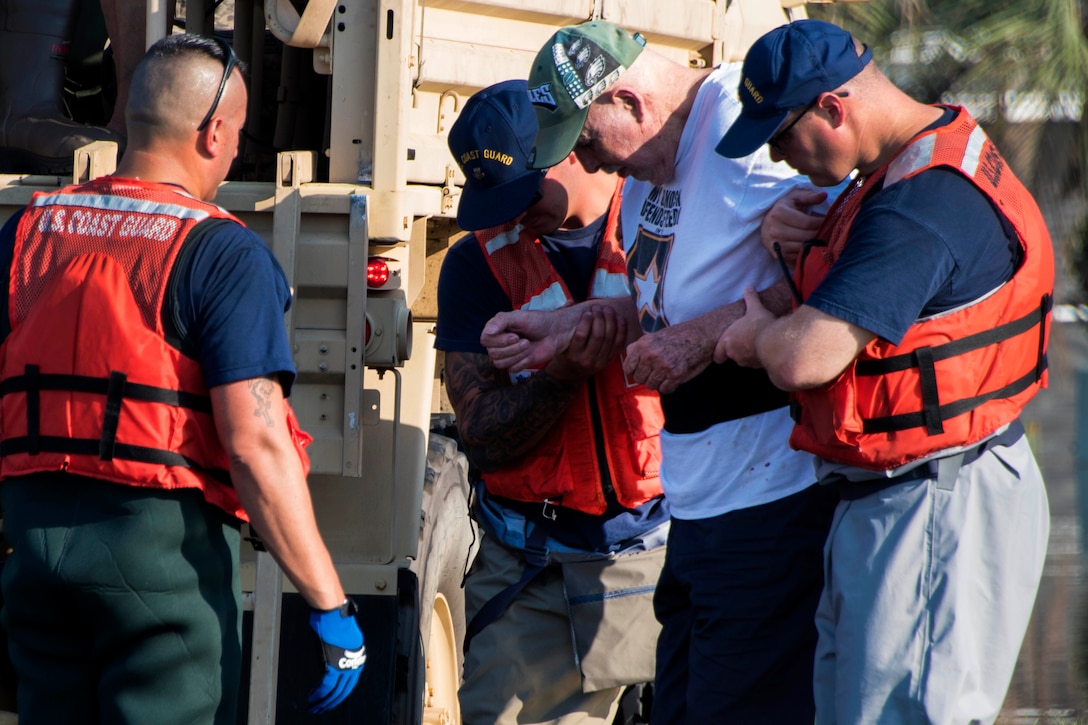 U.S. Coast Guard members assist an elderly man into an Army high-water transport vehicle.