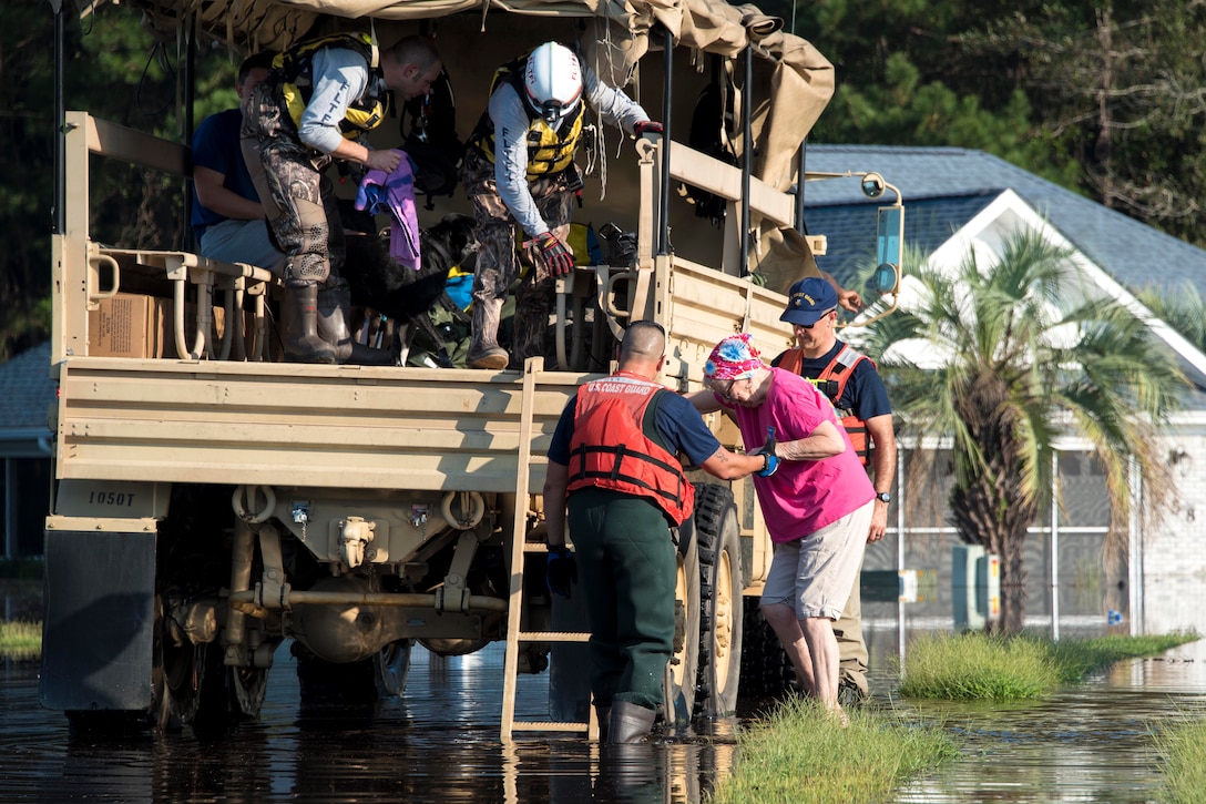 U.S. Coast Guard members assist an elderly woman into an Army high-water transport vehicle.