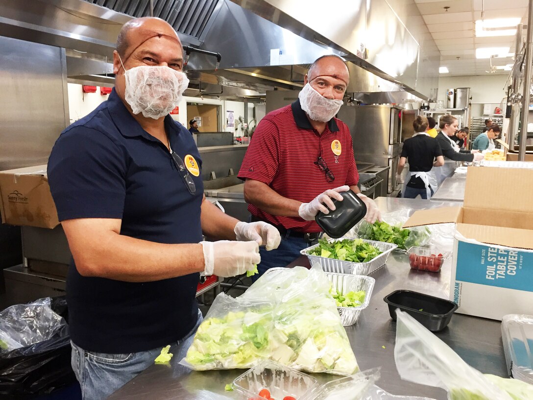 Two male employees wearing gloves prepare salads.