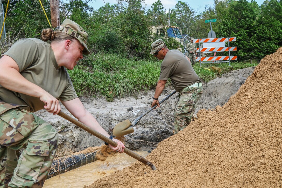 Soldiers use shovels to repair a road damaged by flooding.