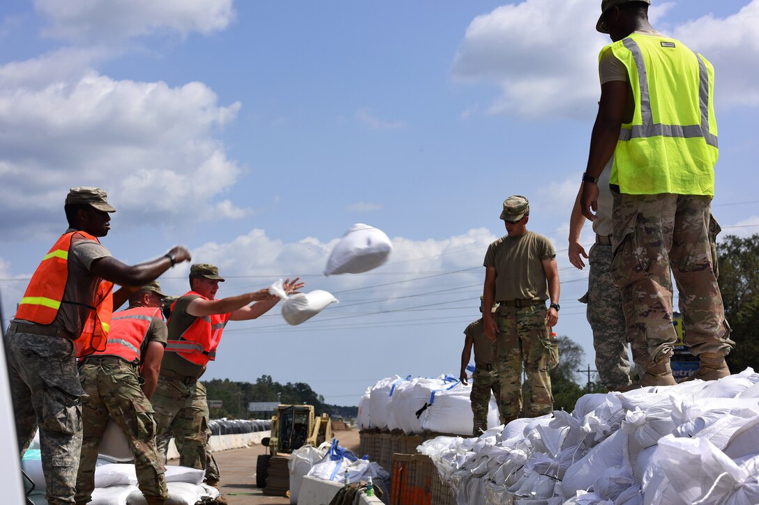 Soldiers toss sandbags to reinforce a flood barrier.