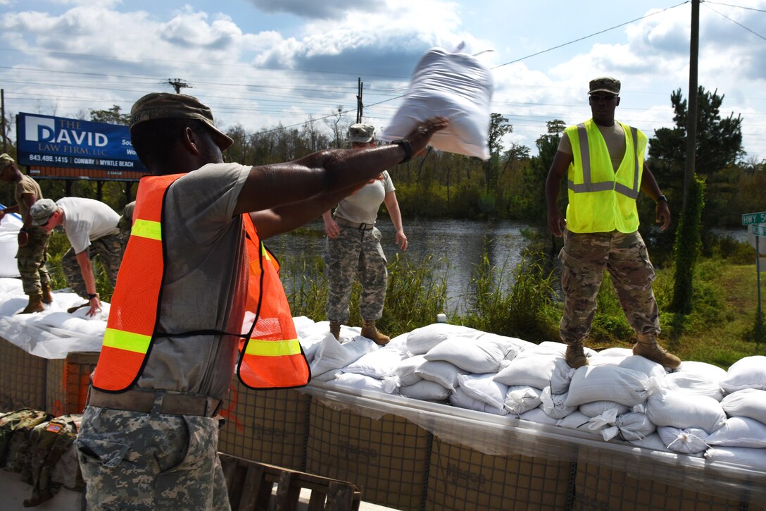 A soldier uses a sandbag to reinforce a flood barrier.