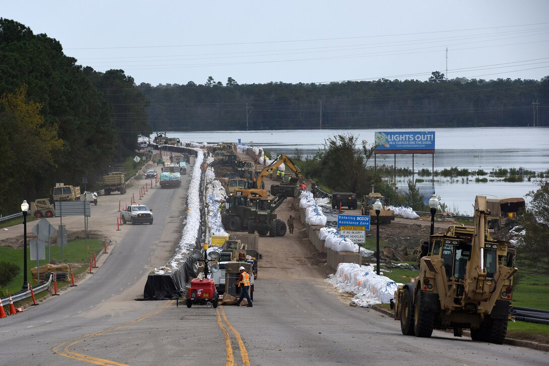Soldiers operate heavy equipment to move bundles of sandbags to reinforce a flood barrier.