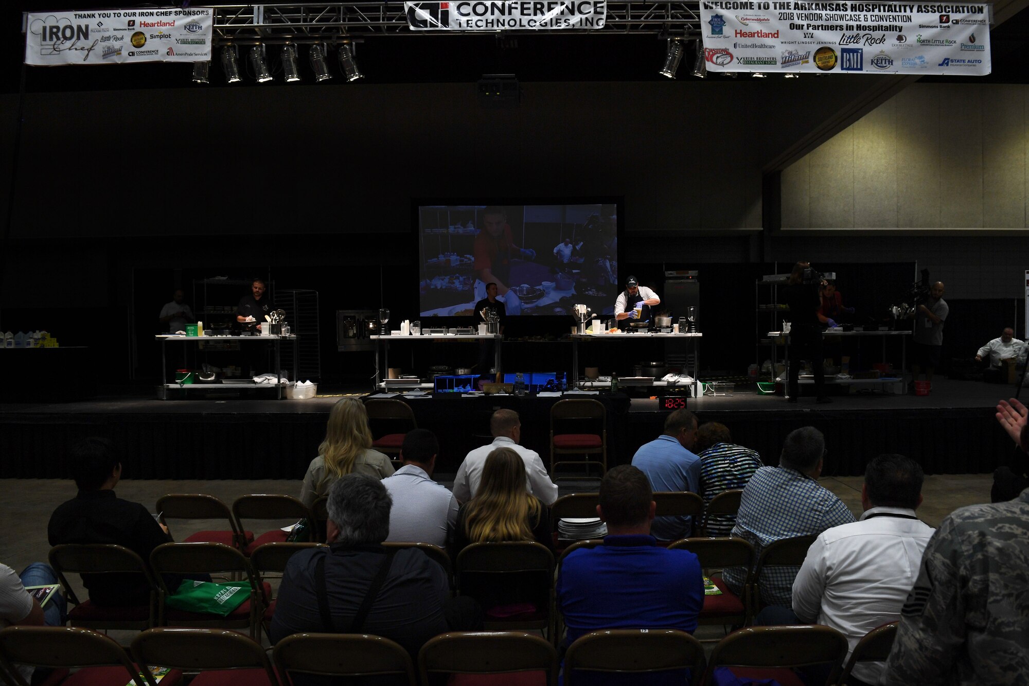 Men cook on top of stage, while people watch.