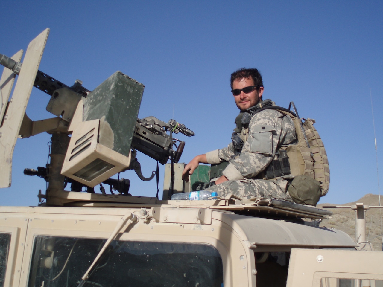 Soldier poses with gun on armored vehicle.