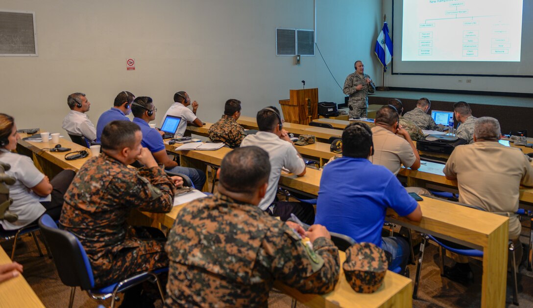 Military members sit at desks during a lecture.