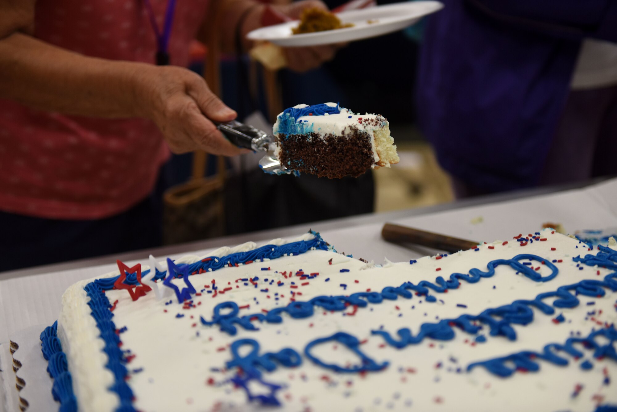 A hand lifts up a piece of marble cake with blue and white frosting.