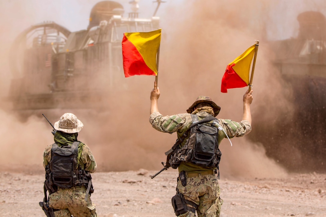 A uses flags to sailor direct an air-cushioned landing craft onto the shore