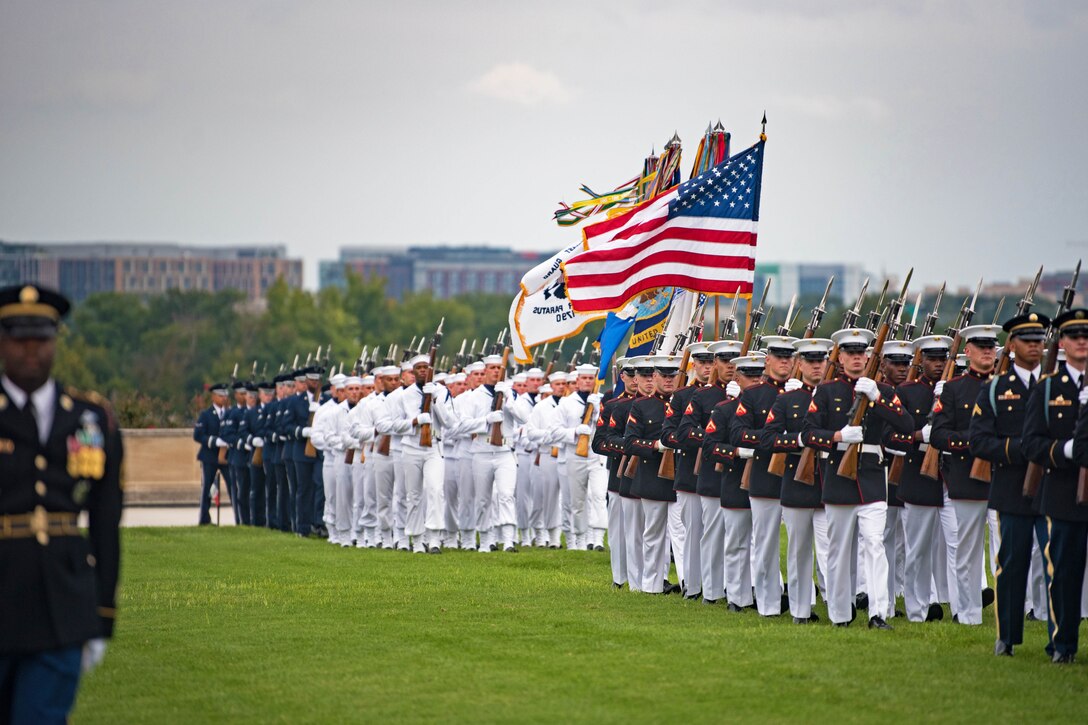 Service members march in formation on a parade field.