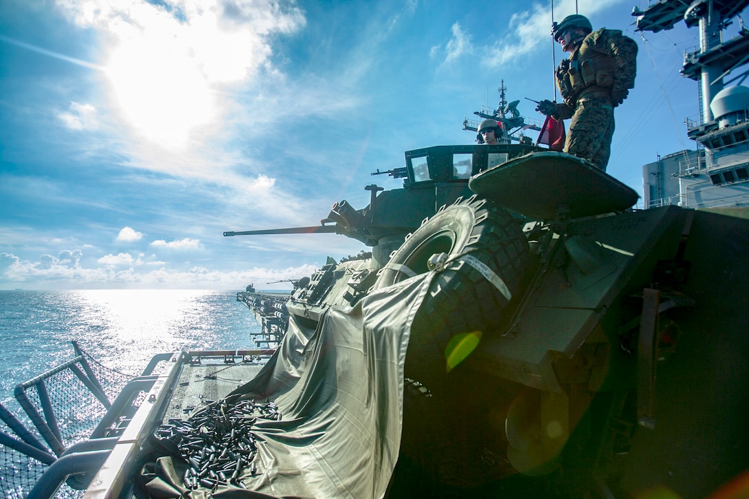 A Marine aims a large gun on the deck of a ship.