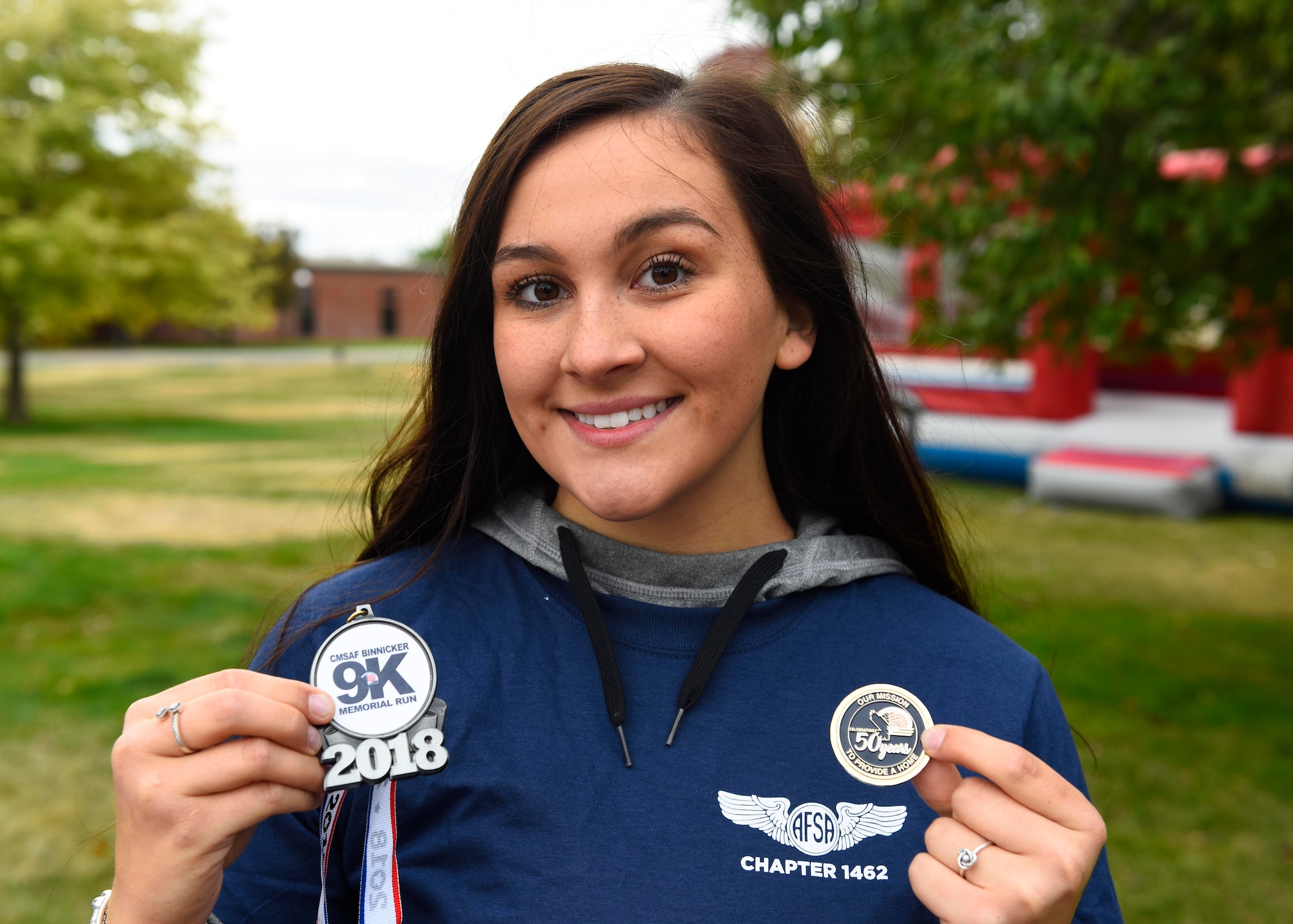Airman Olivia Simione, 92nd Air Refueling Wing Religous Affairs chaplain assistant, poses with the CMSAF Binnicker 9K Memorial Run finisher's medallion and a 50th Anniversary Air Force Enlisted Village commemorative coin at Miller Park in Fairchild Air Force, Washington, Sept. 22, 2018. The AFEV is a nonprofit organization whose core mission is to provide a safe and secure home for survivng spouses of retired enlisted Airmen. (U.S. Air Force photo/Airman 1st Class Lawrence Sena)