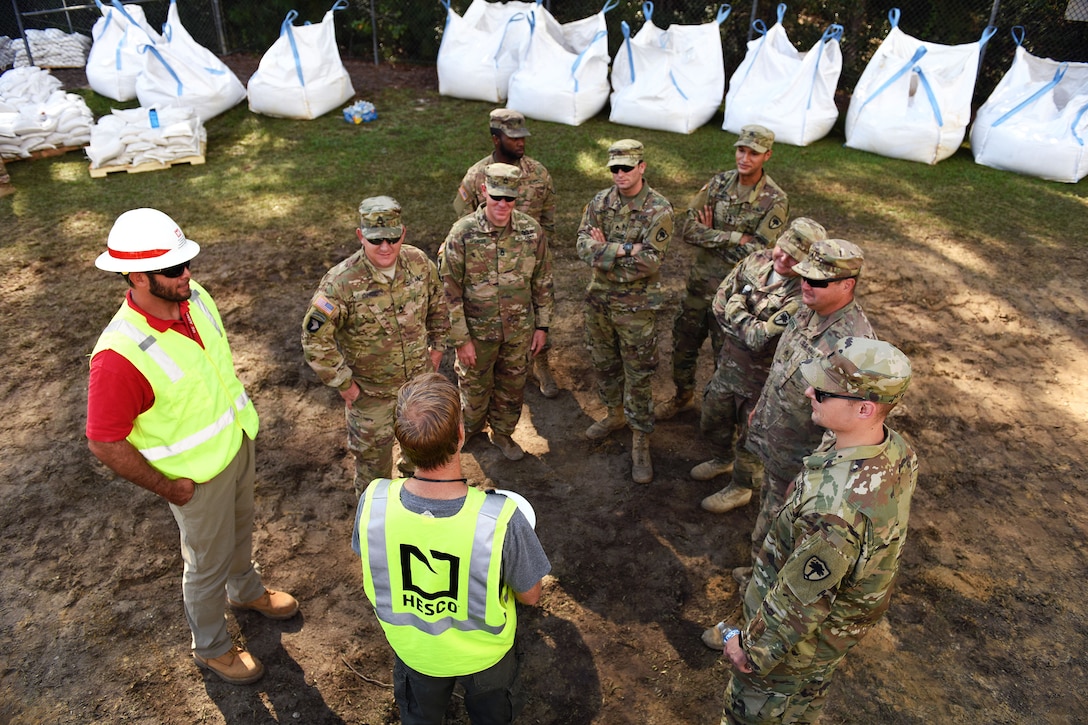 A supervisor gives instructions to soldiers on the proper way to use sand to construct flood water barriers.