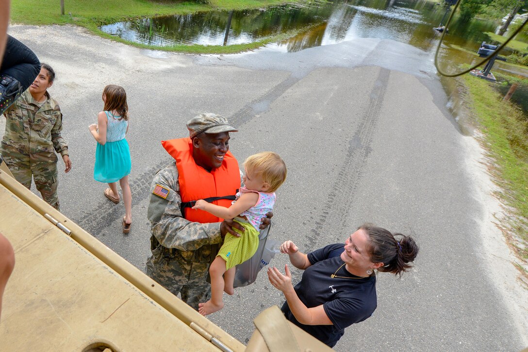 A soldier helps a mother put her daughter onto a transport vehicle.