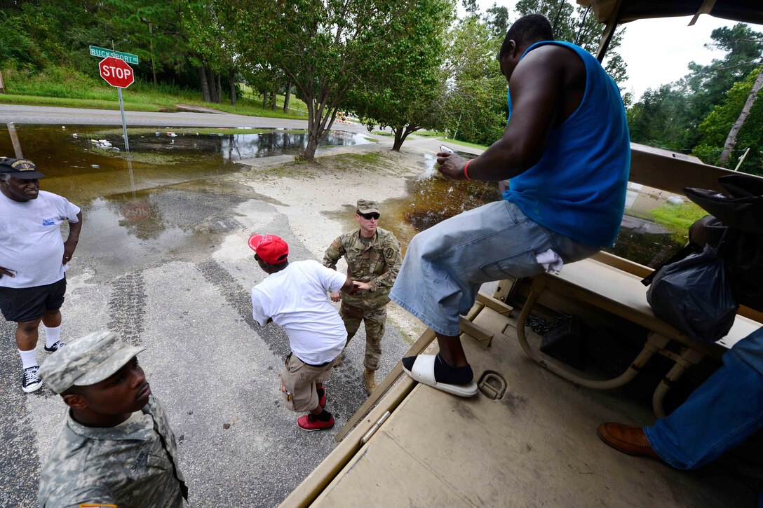 Soldiers help disembark people from a high water vehicle.