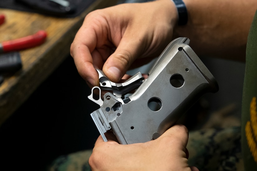 A person's hands work on the butt of a pistol.