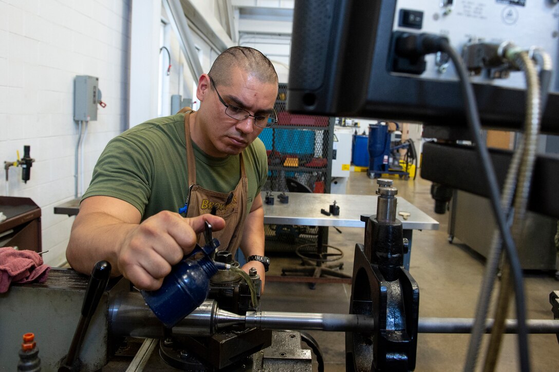 A Marine sits at a work table and oils a lathe.