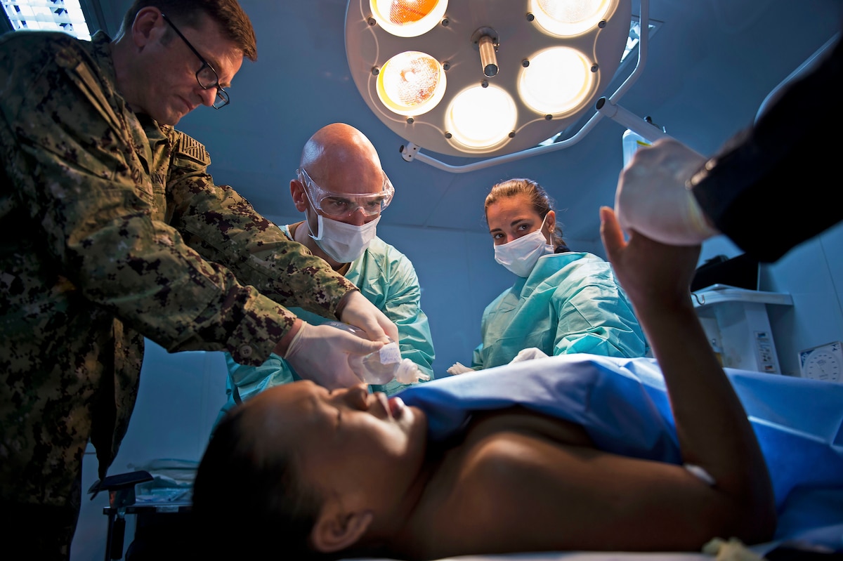 Three service members perform an operation on a patient.