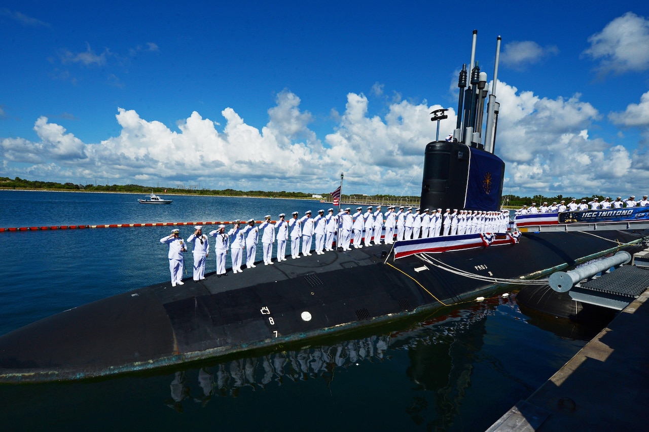 A line of sailors stand atop a submarine.