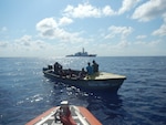 Coast Guard Cutter Hamilton small boat crew boards a suspected smuggling vessel while the Hamilton maintains security in the background March 22, 2019, in the Caribbean Sea.
