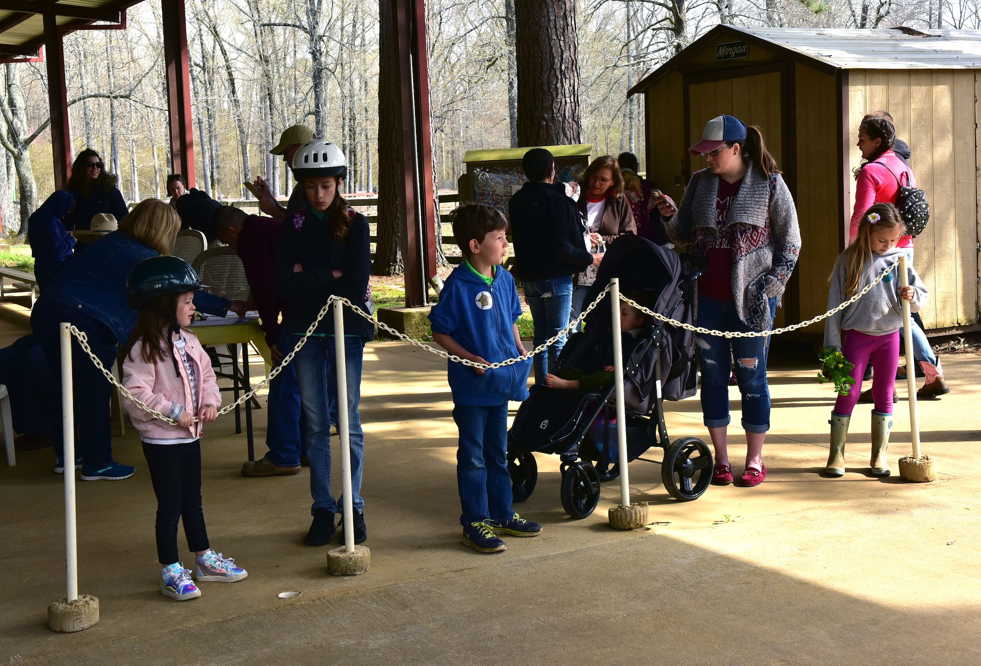 Children and adults line up behind a white chain to ride horses.
